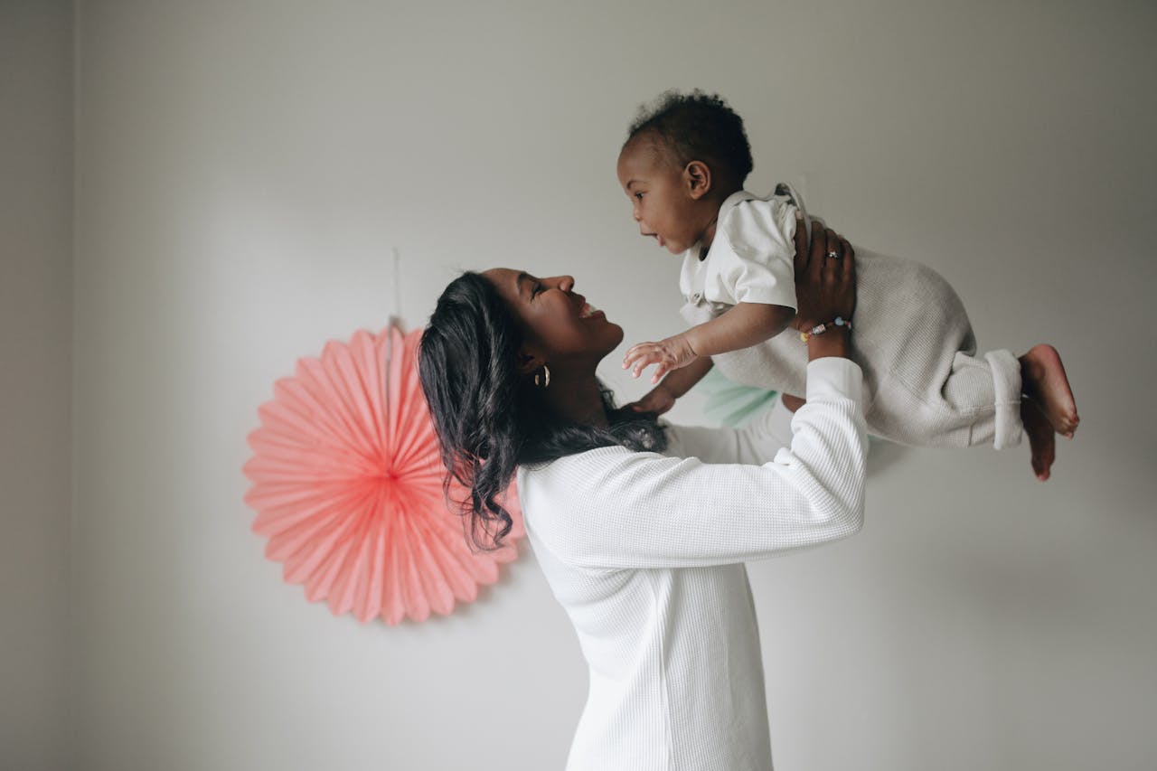 A mother lovingly lifts her baby indoors, capturing a joyful and tender moment.